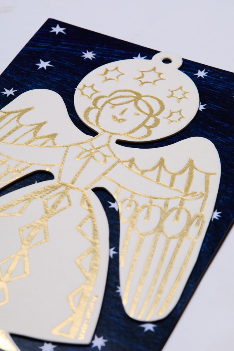 Gold and white letterpress angel christmas decoration on a blue card with white stars