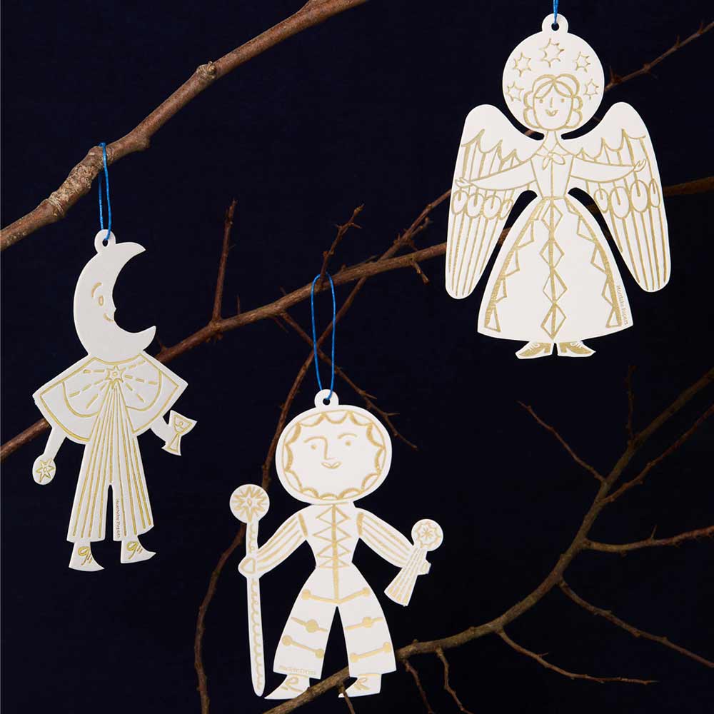 Decorative Christmas ornaments shaped like a moon, a sun, and an angel hanging on a branch against a dark background.