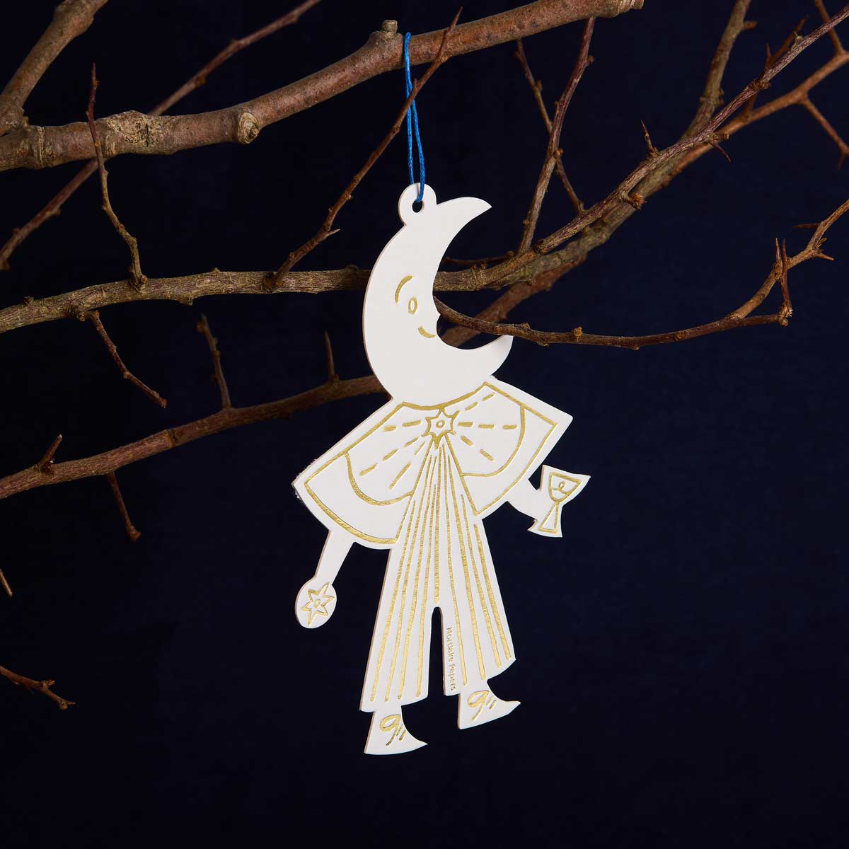 Decorative hanging ornament shaped like a stylized figure with a moon face, holding a glass, against a dark background.