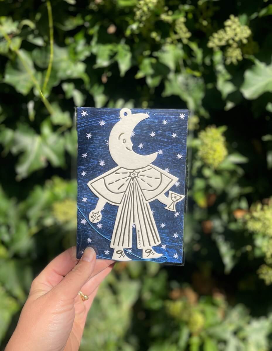 Moon themed decoration in blue and star packaging held in front of green foliage