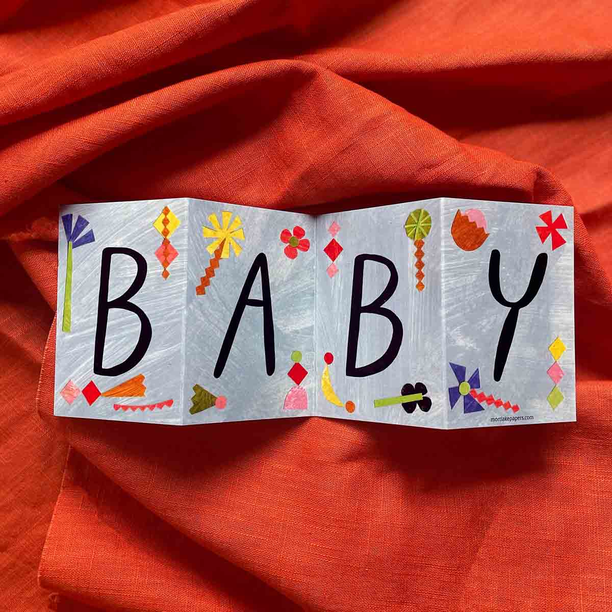 New Baby Concertina Greeting Card, opened to showcase its colorful and artistic design, displayed on a bold red background. A perfect eco-friendly card to celebrate new parents.