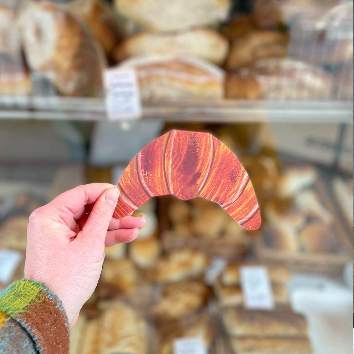 Croissant shaped card held against a British bakery window