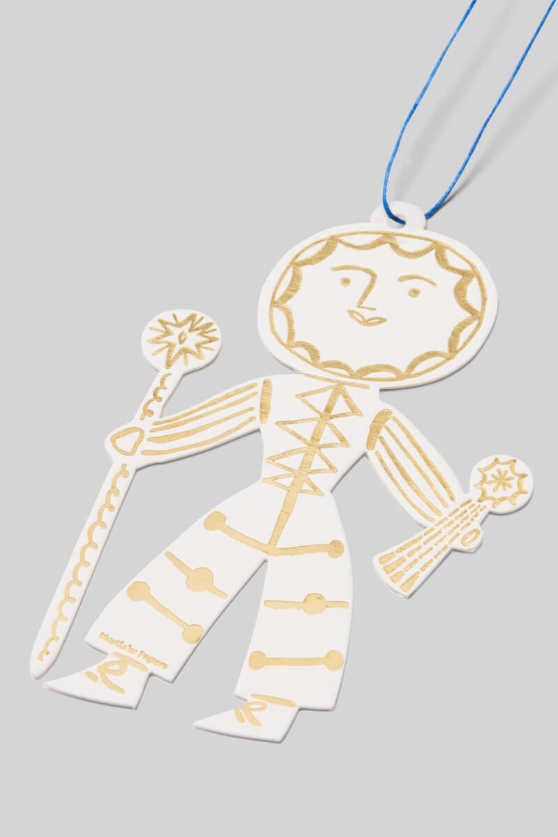 Decorative card cutout of a Sun Folk decoration in gold and white on a gray background.