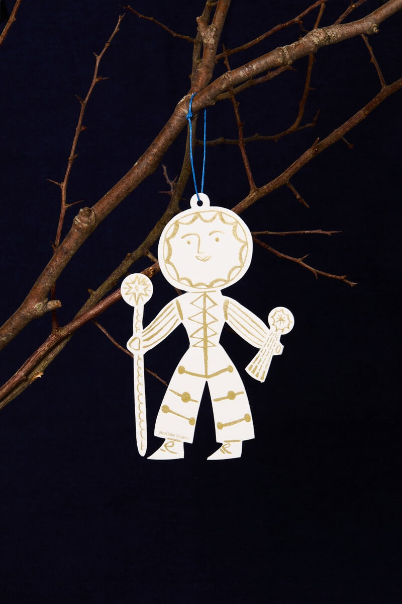 Decorative Sun Folk ornament hanging from a branch against a dark background