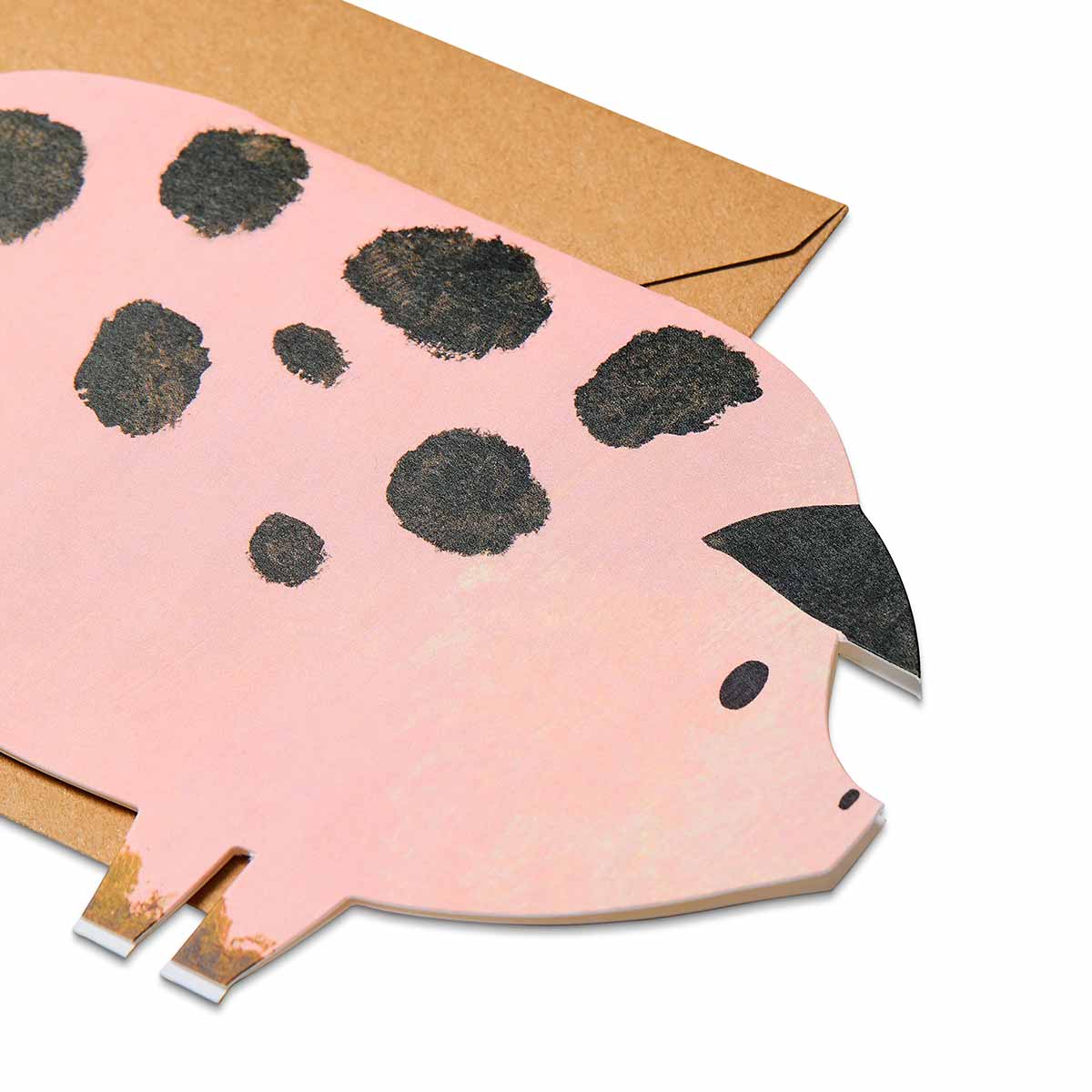 Close up the face of a pig shaped card with black spots on a white background with a brown envelope