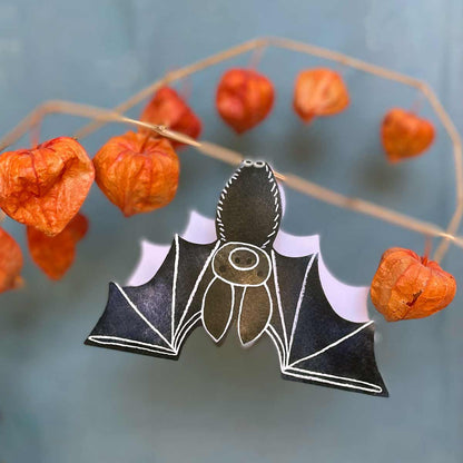 Bat shaped card hanging upside down from a branch of pumpkin coloured branches