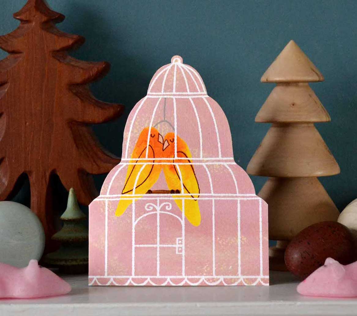 Pink birdcage shaped card with two lovebirds snuggled inside together for love