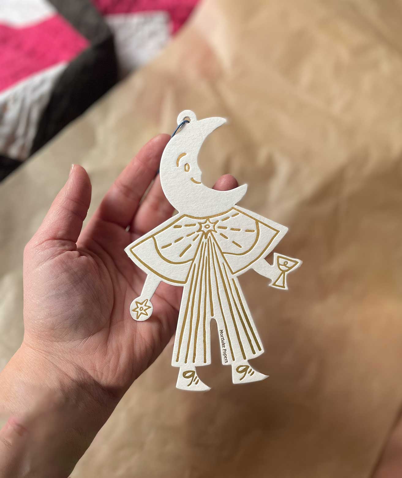 Hand holding a cream and gold moon celestial ornament against a paper background