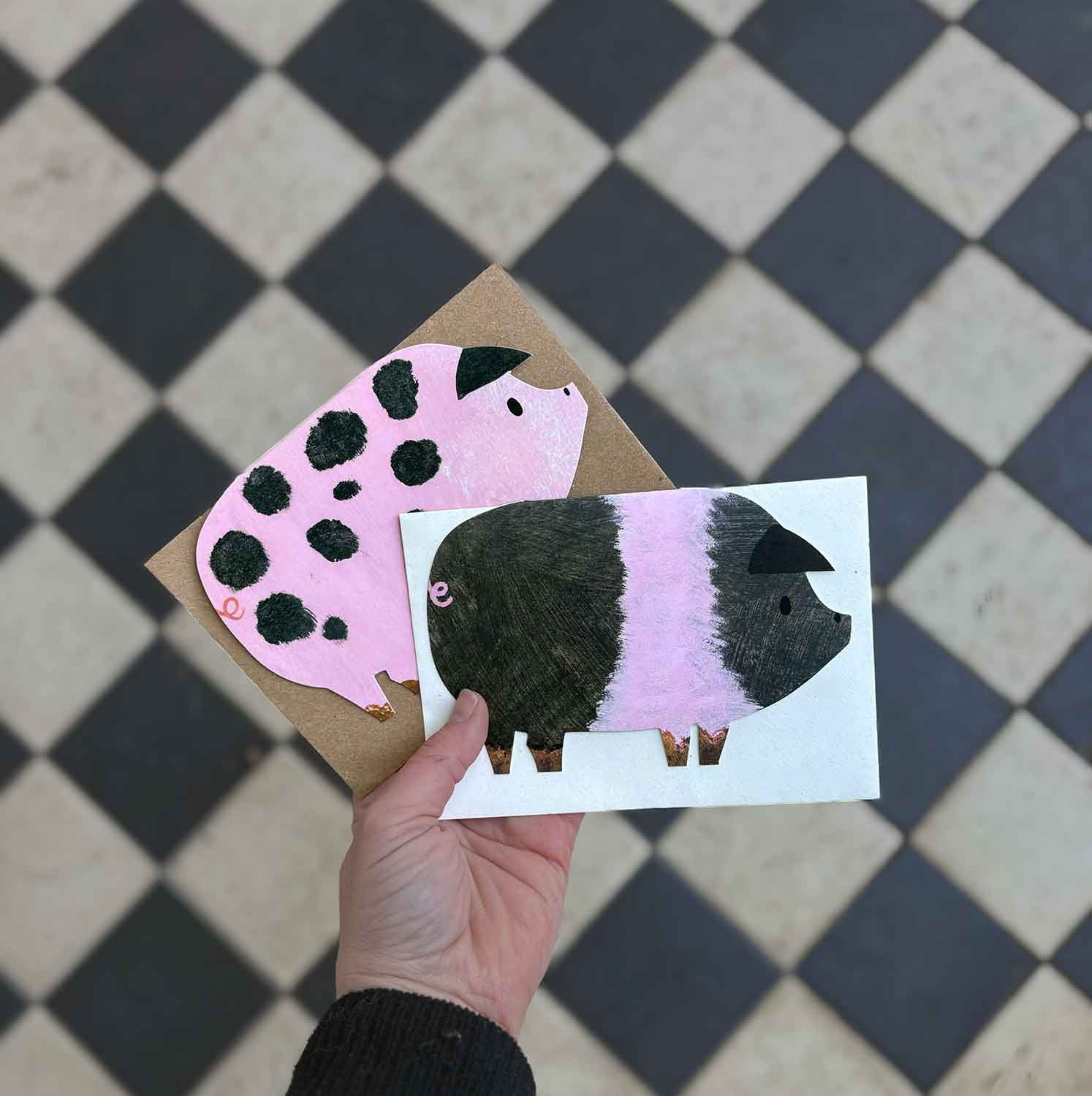 Hand holding a two pig cards against a checkered floor background