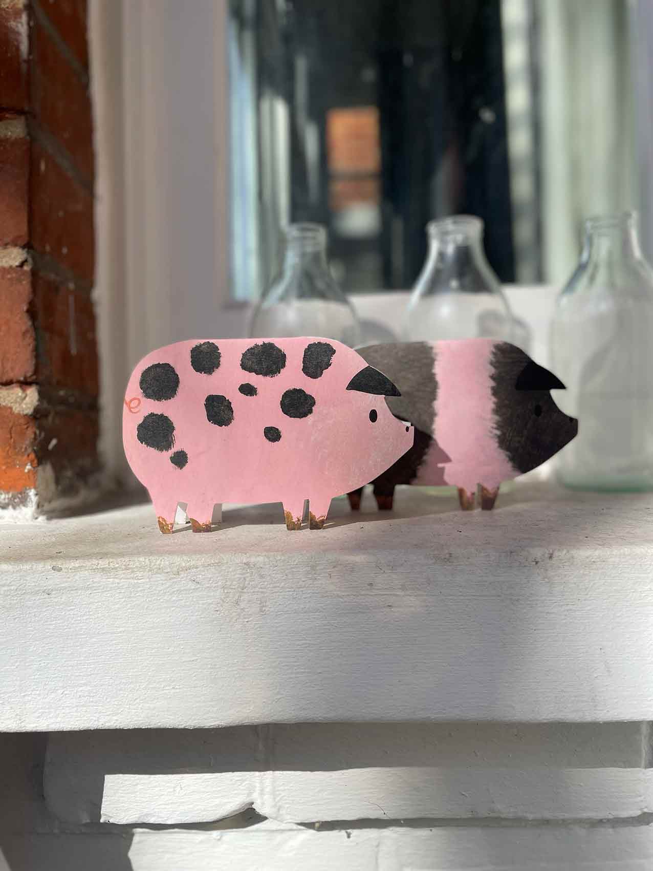Two pig shaped greetings card on a window ledge with a milk bottle behind