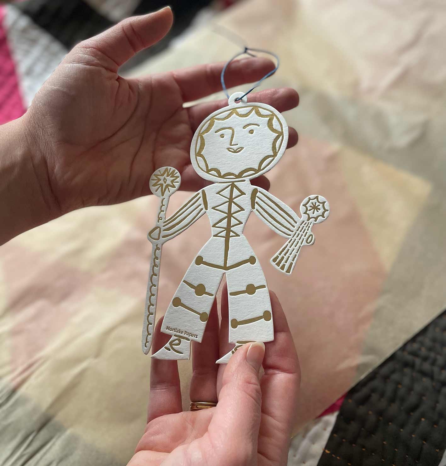 Hand holding a gold and white cutout christmas decoration with a sun design, against a blurred background.