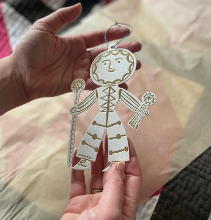 Hand holding a gold and white cutout christmas decoration with a sun design, against a blurred background.