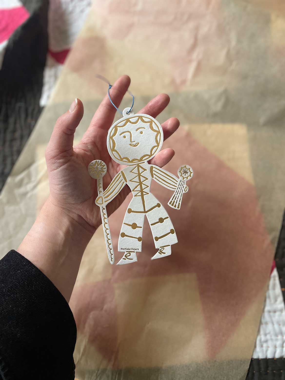 Hand holding a decorative folk sun figure with a checkered background