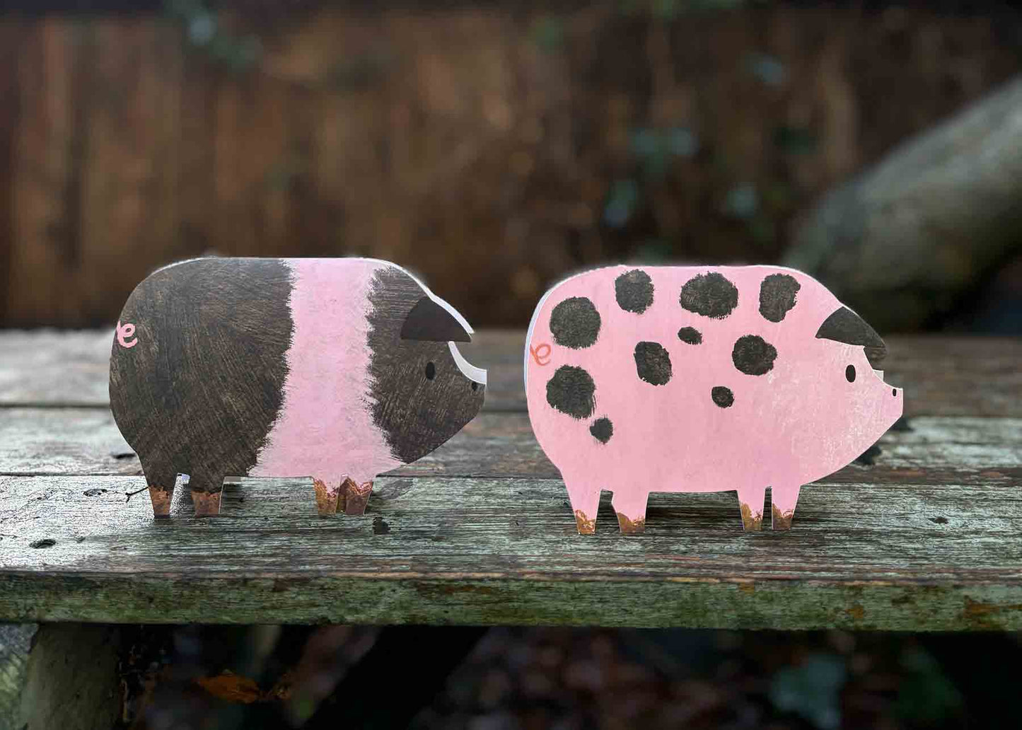 Two die cut pig cards, one black and pink and one pink with black spots, on a wooden surface.