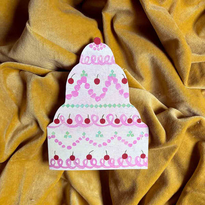 Birthday cake die-cut greetings card with pink frosting and red cherries on a yellow velvet background